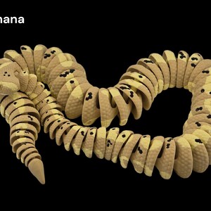 May include: A segmented toy snake in shades of tan and yellow with black spots, resembling a banana. The snake is curved and coiled against a black background. The word "Banana" is in the top left corner.