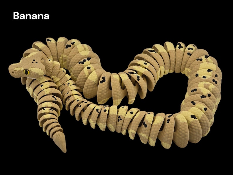 May include: A segmented toy snake in shades of tan and yellow with black spots, resembling a banana. The snake is curved and coiled against a black background. The word "Banana" is in the top left corner.