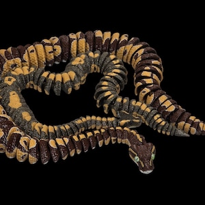 May include: A detailed snake figurine in shades of brown, yellow, and grey, coiled against a black background. The snake's head is visible, with green eyes. The design showcases a patterned skin.