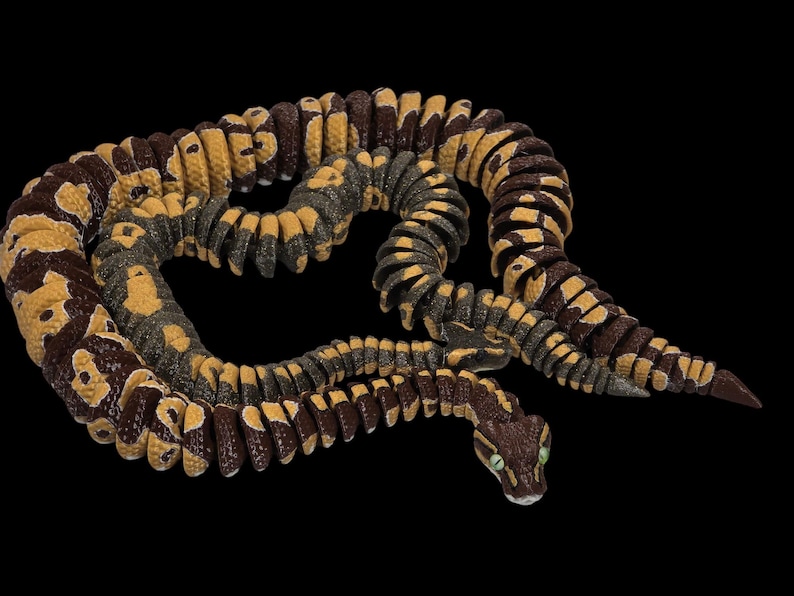 May include: A detailed, coiled snake figurine with a brown, yellow, and gray pattern. The snake's head is visible, featuring green eyes. The background is solid black, highlighting the snake's intricate design.