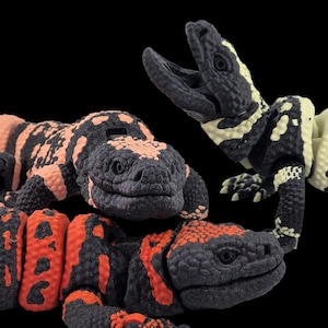 May include: Three toy lizard figurines, one with a black, white and yellow pattern, one with a black, pink and white pattern, and one with a black, red and white pattern.
