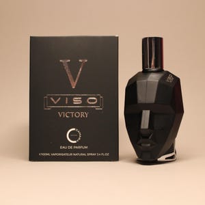Puede incluir: Un juego de botella y caja de perfume negro. La botella tiene un diseño geométrico y una tapa plateada. La caja negra lleva la palabra "VISO VICTORY" en plata. La botella contiene 100 ml de perfume.