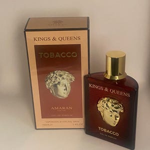 Puede incluir: Una botella de Eau de Parfum "Kings & Queens Tobacco" con tapón dorado y caja a juego. La botella y la caja presentan un diseño de busto dorado y el texto "TOBACCO". La botella contiene 100 ml de perfume.