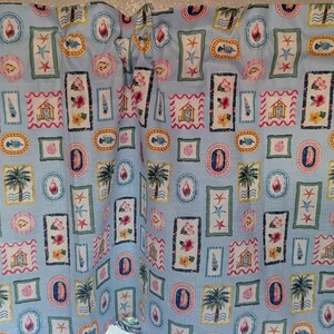 May include: Light blue fabric with a repeating pattern of framed beach scenes, including palm trees, starfish, seashells, and fish. The frames are in various shapes and colors, creating a coastal theme. The fabric is likely used for curtains or other home decor.