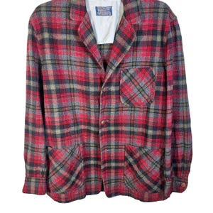 May include: A long-sleeve blazer featuring a red, black, and grey plaid pattern. The garment includes a notched lapel, a single chest pocket, two lower front pockets, and three front buttons. A white interior label reads Pendleton.