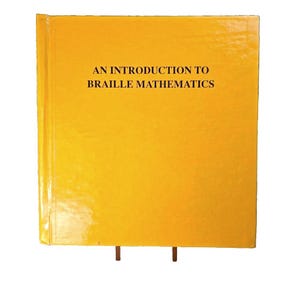 Puede incluir: Un libro de tapa dura de color amarillo brillante con el título AN INTRODUCTION TO BRAILLE MATHEMATICS impreso en letras mayúsculas negras en la portada. El libro está colocado en posición vertical, mostrando una superficie lisa y un lomo.