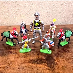 May include: A collection of plastic toy figures featuring a central knight in silver armor with a black chest plate displaying a yellow dragon, surrounded by mounted knights on black horses and foot soldiers holding spears and shields with colorful accents.