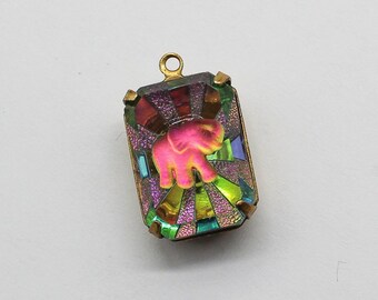 May include: A colorful iridescent glass pendant featuring a pink elephant design. The pendant has a gold-toned metal bail for attaching to a chain or cord.