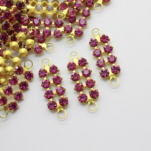 May include: A group of gold-toned metal embellishments with pink rhinestones. Each embellishment has two loops at the top and features a row of rhinestones.