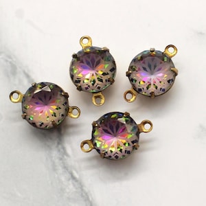 Könnte beinhalten: Vier runde, irisierende Kristallverbinder mit goldfarbenen Metalleinfassungen. Die Kristalle zeigen eine Reihe von Farben, darunter Lila, Rosa und Gelb. Jeder Verbinder hat zwei Schlaufen zur Befestigung. Die Verbinder liegen auf einer weiß-grauen Marmoroberfläche.