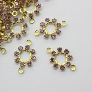 May include: Three gold-toned metal charms with a circular design. Each charm features a ring of small, light purple rhinestones.