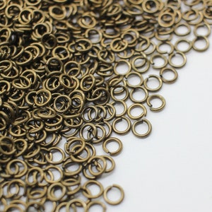 May include: A large pile of small, gold-colored jump rings. The rings are arranged in a loose pile, with some of the rings overlapping.
