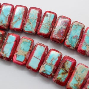 May include: Two parallel strands of rectangular beads featuring a vibrant red border surrounding a central inlay of bright turquoise stone with intricate brown and tan veining. Each bead has a smooth, polished finish and rounded corners.