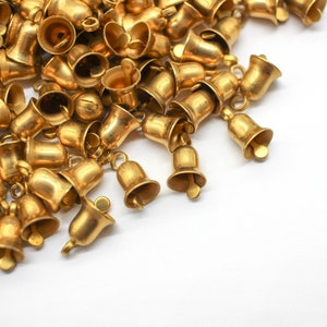 May include: A large pile of gold-colored jingle bells, scattered on a white surface.
