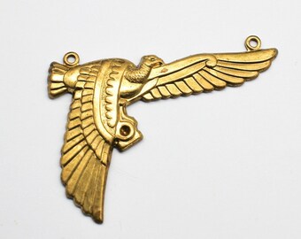 May include: A gold-colored metal pendant shaped like a stylized bird with outstretched wings. The pendant has two holes for attaching a chain or cord.