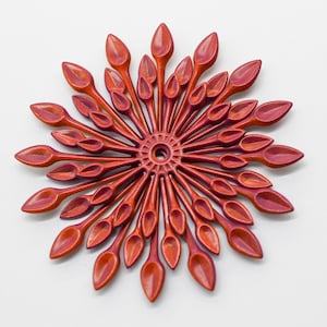 May include: A red and orange metal flower-shaped wall decor with a circular center and multiple petals.