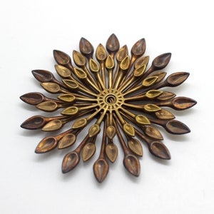 May include: A gold and brown metal sunburst wall decor with a circular center and radiating spokes with leaf-shaped ends.