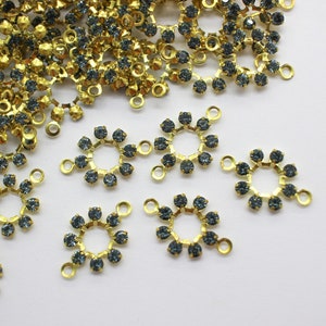 May include: A close-up of a pile of gold-toned metal charms with blue rhinestones. The charms are in the shape of a circle with a small loop at the top.