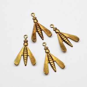 May include: Four antique gold-colored bee charms. Each charm features a detailed body, wings, and a small loop at the top for attaching to jewelry or other crafts. The charms are arranged on a white background.