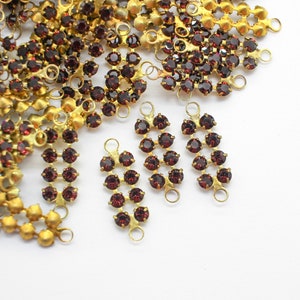 Può includere: Primo piano di componenti di gioielleria con catene in metallo dorato e gruppi di strass rosso scuro. Diversi gruppi di strass sono disposti in un design a cascata, perfetto per orecchini o altri progetti di gioielleria.