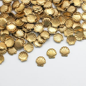 May include: A large pile of gold-colored metal seashells on a white background. The seashells are scattered randomly and some are overlapping.