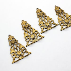 May include: Four gold-colored metal filigree ornaments in the shape of a triangle. The ornaments have a delicate, intricate design with floral motifs.