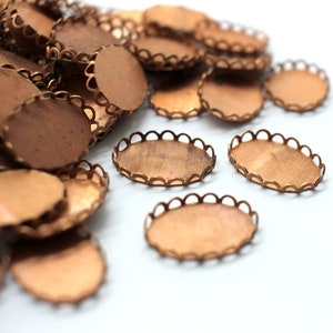 May include: A pile of oval-shaped, copper-colored metal settings with scalloped edges. The settings are used for crafting jewelry or other decorative items.