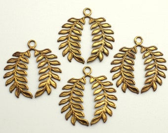 May include: Five gold-colored leaf-shaped pendants with a loop at the top for hanging. The pendants are arranged on a white surface. Each pendant has detailed leaf veins.