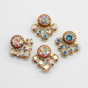 May include: Three gold-toned metal embellishments with iridescent rhinestones. Each embellishment features a round center stone surrounded by smaller stones in a teardrop shape.