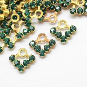 May include: A pile of gold-toned metal embellishments with green crystal accents. Each embellishment has a loop at the top and a row of crystals along the bottom.