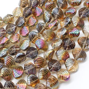 May include: A collection of iridescent, shell-shaped beads in shades of brown, gold, and purple. The beads have a textured, ridged surface and are strung together, ideal for jewelry making or crafting projects.