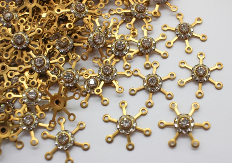 May include: A pile of gold-toned metal snowflake charms with clear rhinestone accents.