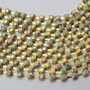 May include: A gold chain with iridescent rhinestones. The chain is made of small, square-shaped rhinestones that are set in a gold metal frame. The rhinestones are arranged in rows and are connected by small gold metal links.