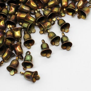 May include: A large group of small, gold-toned bells with a shiny, metallic finish. The bells are scattered on a white surface.