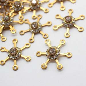 May include: A group of gold-toned metal charms with clear rhinestone accents. Each charm has six arms and a central rhinestone.