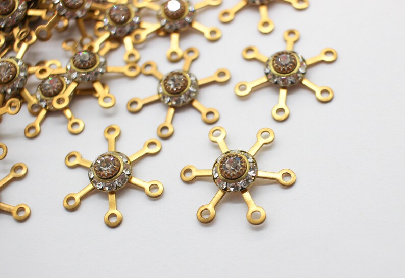 May include: A group of gold-toned metal charms with clear rhinestone accents. Each charm has six arms and a central rhinestone.