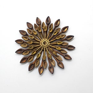 May include: A gold and brown metal wall sculpture with a circular design. The sculpture is made up of many small, pointed pieces that radiate outwards from the center.