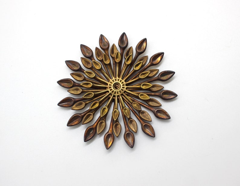May include: A gold and brown metal wall sculpture with a circular design. The sculpture is made up of many small, pointed pieces that radiate outwards from the center.