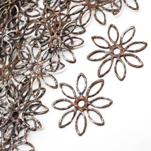 May include: A pile of rusty metal flower shapes, with a few individual shapes scattered on a white background.