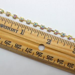 May include: A gold chain with iridescent square rhinestones, measuring 3 inches long. The chain is shown next to a ruler.
