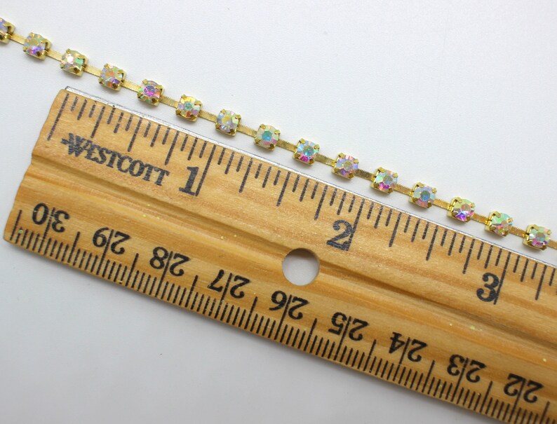 May include: A gold chain with iridescent square rhinestones, measuring 3 inches long. The chain is shown next to a ruler.