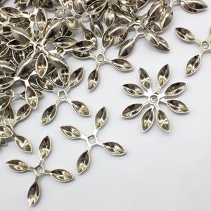May include: A pile of silver metal flower-shaped embellishments with five petals each. The embellishments have a hole in the center for attaching to a project.