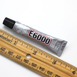 May include: A silver tube of E6000 industrial strength adhesive with a black cap. The tube is 2 inches long and is next to a wooden ruler.