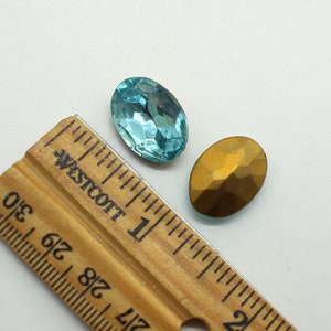 May include: Two oval-shaped rhinestones, one is a light blue color and the other is a gold color. The rhinestones are next to a ruler with the text "Westcott" printed on it.