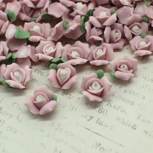 May include: A collection of small, pink rose-shaped embellishments with white centers and green leaves. These decorative floral accents are scattered across a vintage paper background, perfect for craft projects.