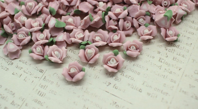 May include: A collection of small, pink rose-shaped embellishments with white centers and green leaves. These decorative floral accents are scattered across a vintage paper background, perfect for craft projects.