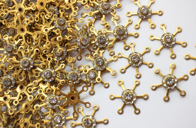 May include: A pile of gold-toned metal snowflake charms with clear rhinestone accents.