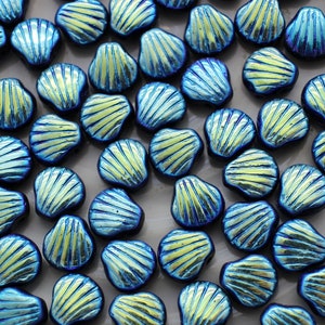 May include: A collection of iridescent blue seashell-shaped beads. Each bead has a textured surface with radiating lines and a yellow-green center. The beads are scattered across a neutral surface, creating a visually appealing pattern. Ideal for jewelry making.