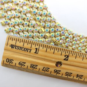 May include: A close-up of gold rhinestone chain trim with iridescent stones. The chain is measured against a ruler, showing it is approximately 2 inches long.
