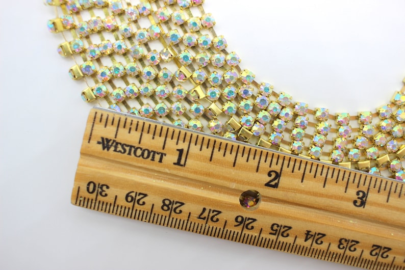 May include: A close-up of gold rhinestone chain trim with iridescent stones. The chain is measured against a ruler, showing it is approximately 2 inches long.